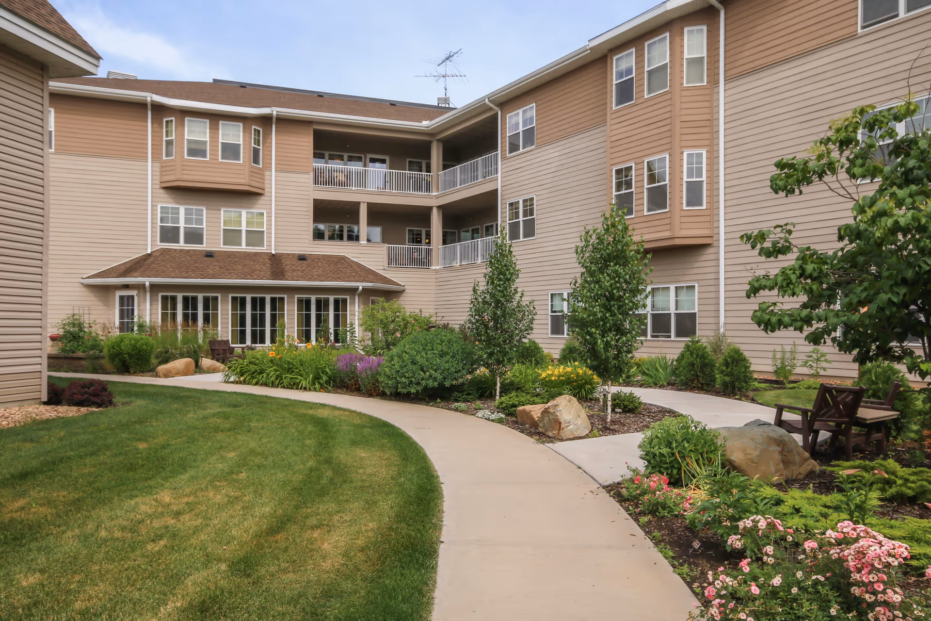 Landscaped courtyard with a curved walkway, benches, and a multi-story senior living building with balconies.