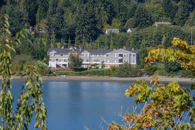 A large, multi-story assisted living facility named Liberty Shores Assisted Living situated near a body of water with trees and greenery surrounding the area.
