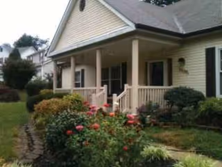 Front view of a single-story assisted living building with a porch and blooming garden.