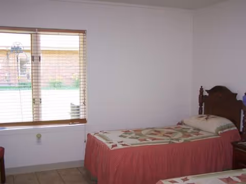 A bedroom in a senior living facility with a bed, quilts, and a window view