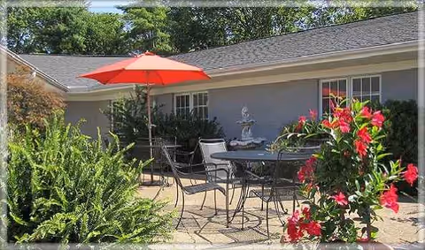 Outdoor patio area at Heritage Center with table, chairs, red umbrella, and plants.