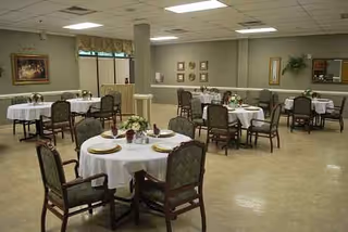 A spacious dining room with round tables set with white tablecloths and chairs.