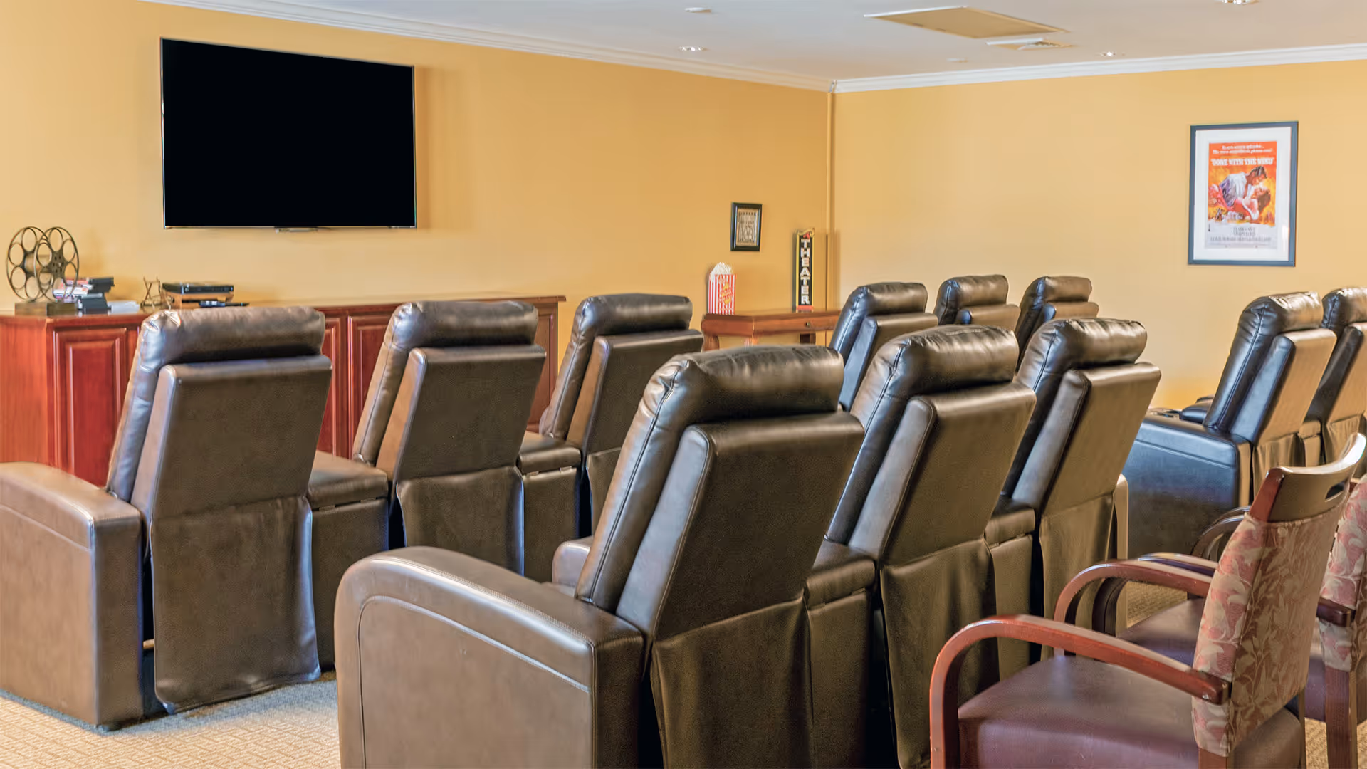 Rows of leather recliner chairs arranged theater-style facing a wall-mounted television in a common room.