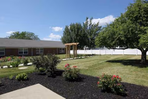 Exterior view of Maplewood of Shanes Village with lawn, garden beds, and a wooden pergola.