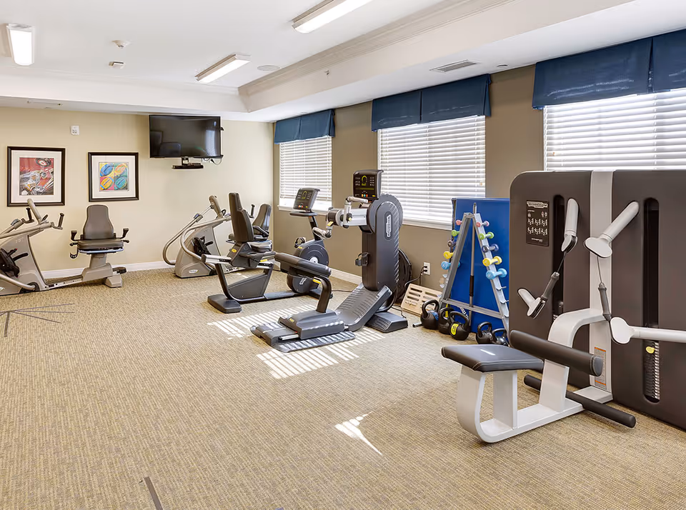 Bright fitness room with exercise equipment including recumbent bikes, a treadmill, weight machines, and free weights.