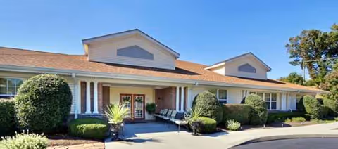 Single-story senior living facility front entrance with shrubs, benches, and manicured landscaping.