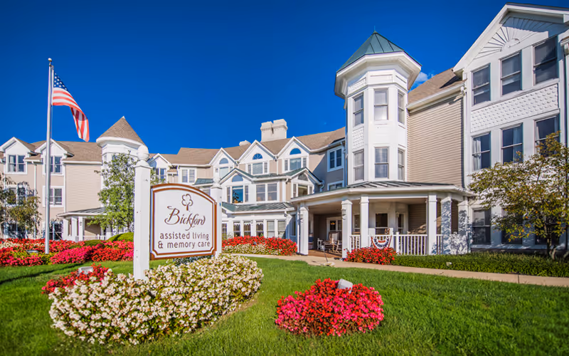 White multi-story assisted living building with a Bickford sign and manicured landscaping.