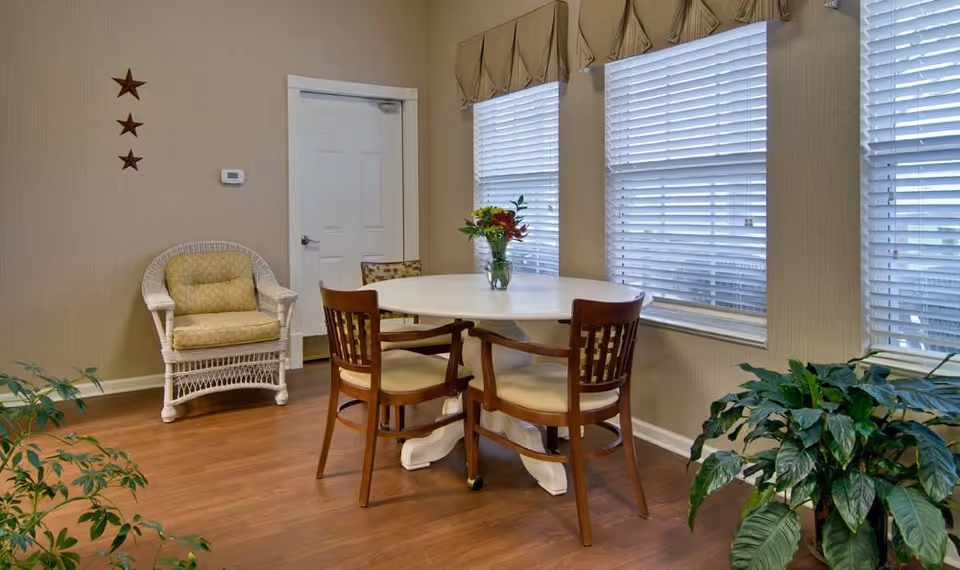 Cozy dining room with round table, wooden chairs, wicker chair, blinds, and plants