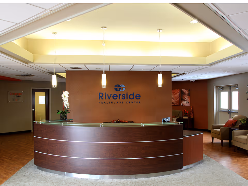 Curved wood reception desk and waiting area inside Riverside Healthcare Center with pendant lights and seating.