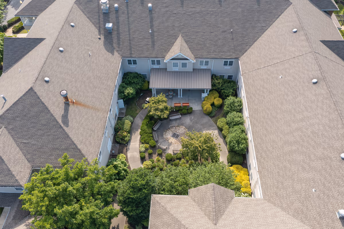 Aerial view of a landscaped central courtyard with walkways, benches, shrubs and trees surrounded by the building's pitched roofs.