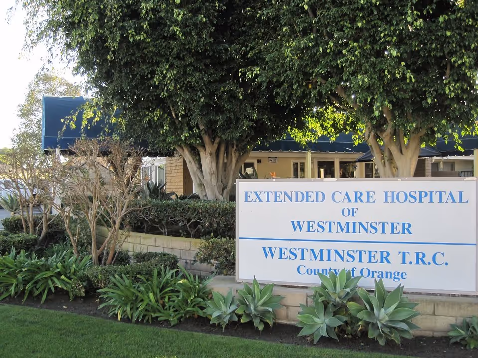 Entrance sign reading 'Extended Care Hospital of Westminster' surrounded by trees and landscaped shrubs in front of the facility.
