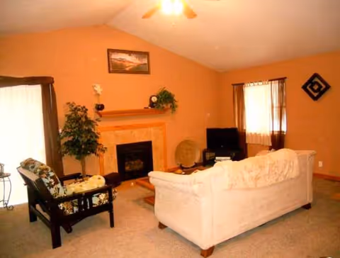 Cozy living room with sofa, chairs, fireplace, plants, and a TV.