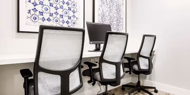 Interior office area with mesh-backed chairs, a computer, and blue patterned artwork.