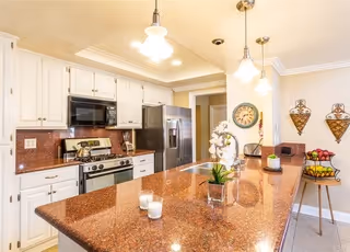 Bright kitchen with a large brown island countertop, white cabinets, stainless steel appliances, pendant lights, and decorative wall accents.