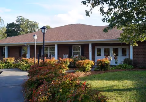 Single-story brick senior living facility with front entrance, walkway, lawn, and shrubs.
