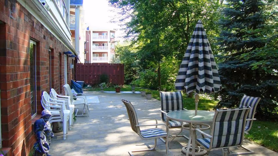 Outdoor patio beside a brick building with a glass table, striped umbrella and several chairs.