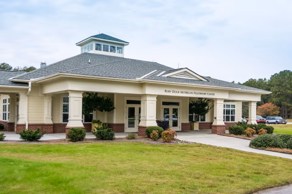 Front exterior of a single-story retirement community building labeled "Ruby Doub McMillan Fellowship Center" with a covered entrance and landscaped lawn.