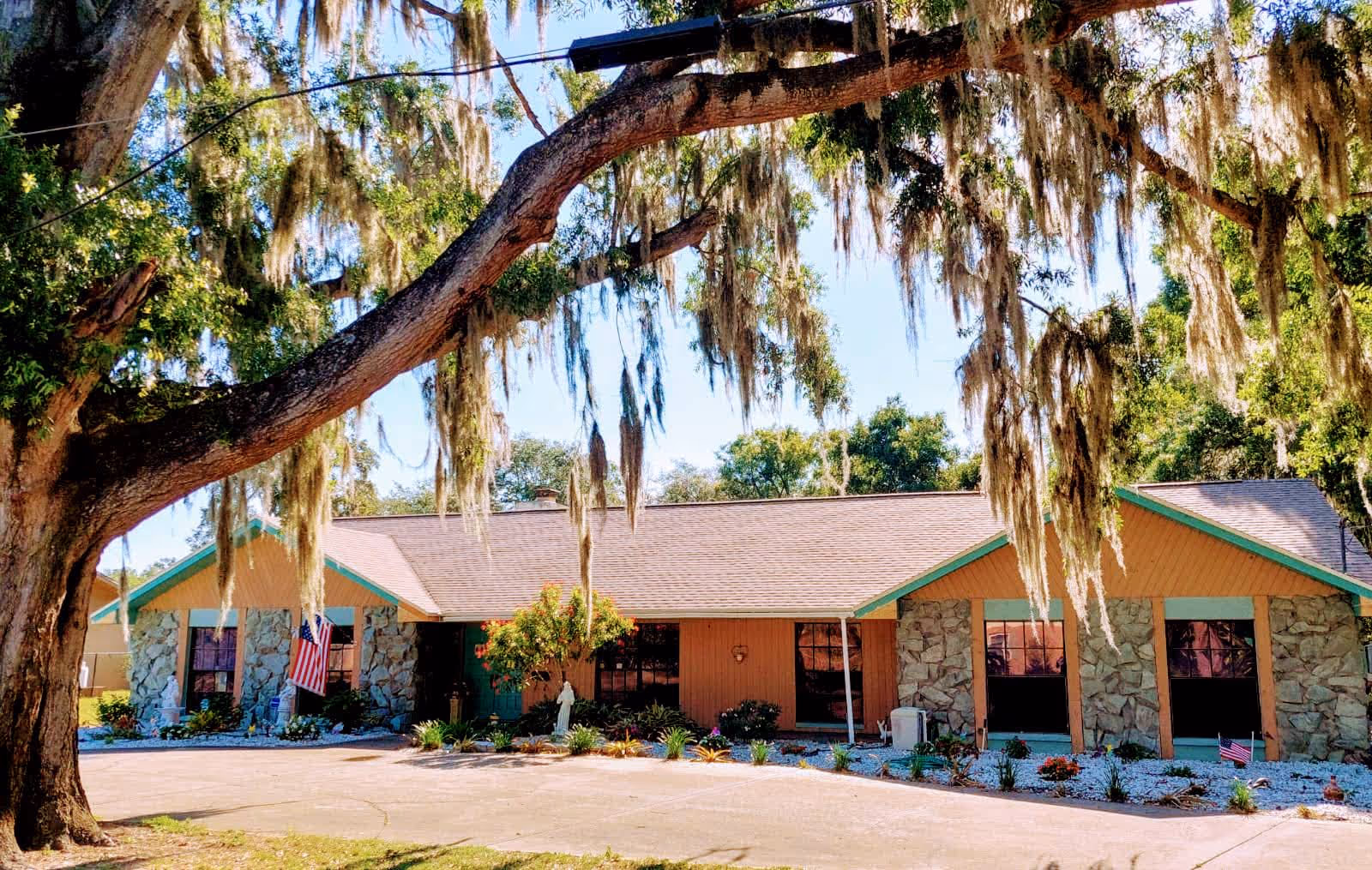 Front exterior of a single-story facility with stone accents, an American flag, and a large oak tree draped in Spanish moss.