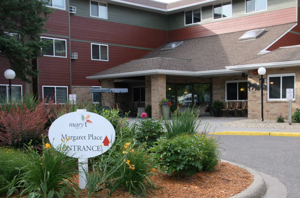 Exterior view of Margaret Place senior living entrance with landscaped shrubs and sign.