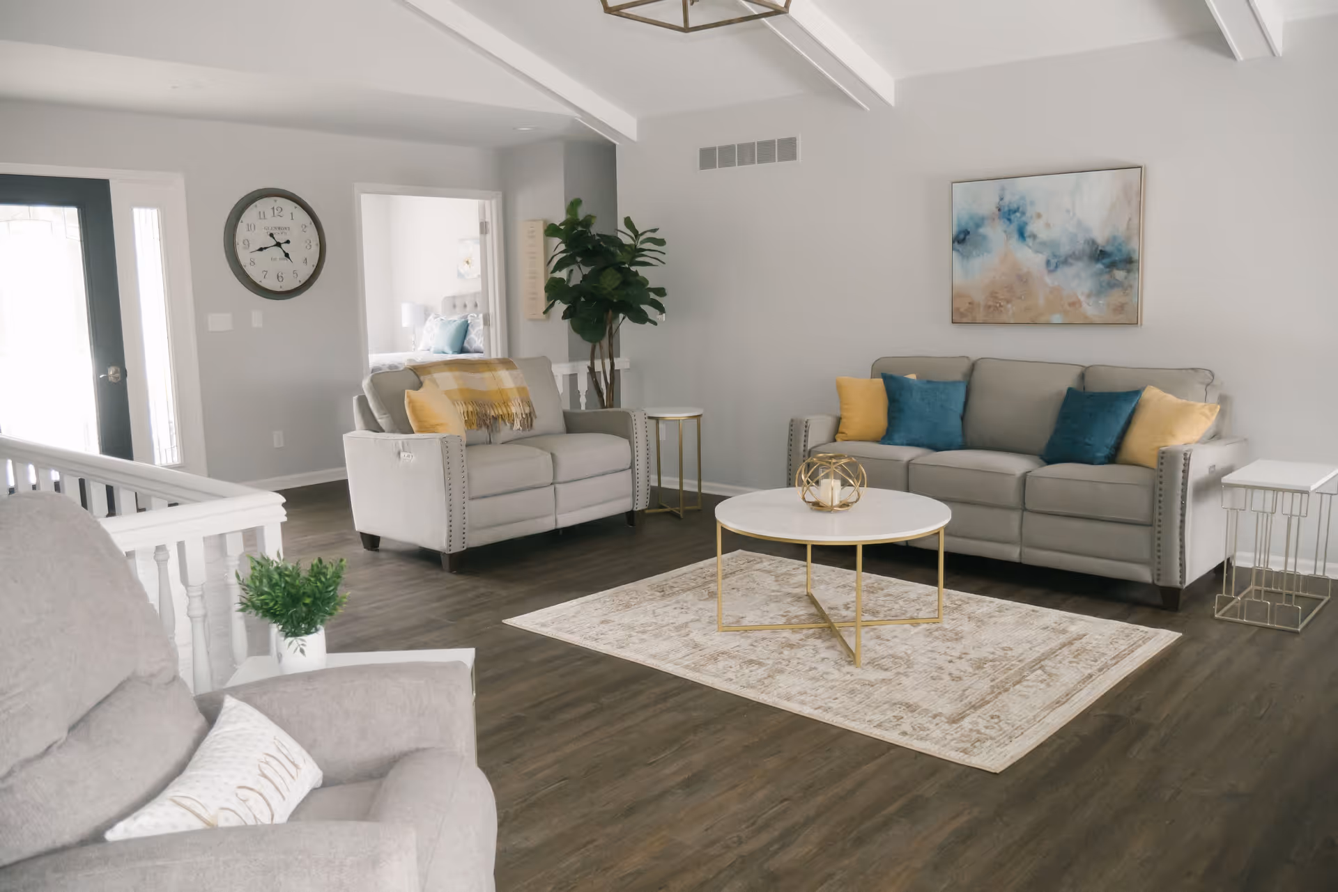 Light-filled living room with gray sofas, colorful throw pillows, a round coffee table on a rug, and wall art.