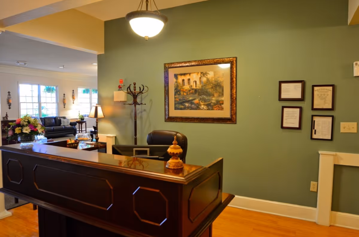 Reception desk and seating area in a senior living facility lobby with framed artwork on a green wall.