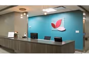 Reception desk in a senior living facility with a teal accent wall and a three-leaf logo mounted behind it.