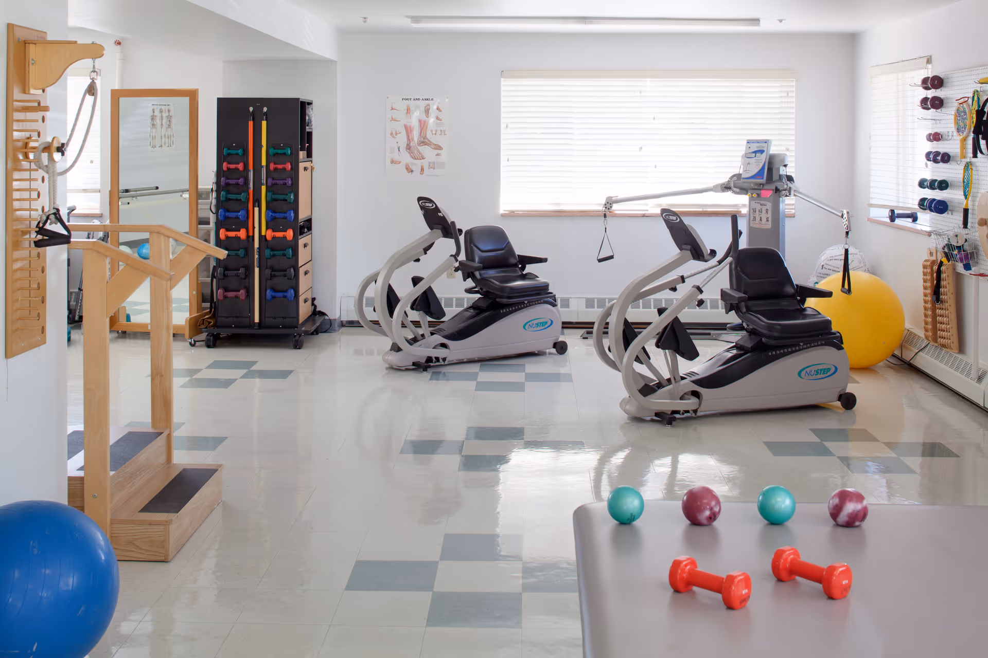 A bright physical therapy/exercise room with two recumbent exercise bikes, hand weights, exercise balls and rehabilitation equipment.