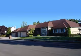 Front view of The GoodLife Adult Family Home exterior with driveway and well-manicured lawn.