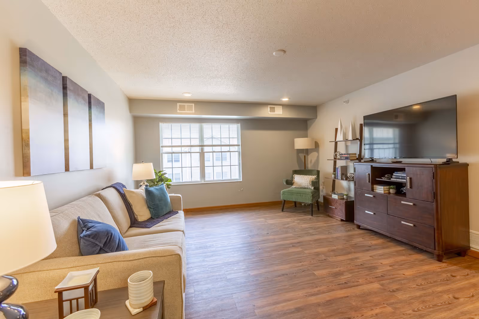 Bright furnished living room with a sofa, armchair, large window and a TV on a wooden media console.