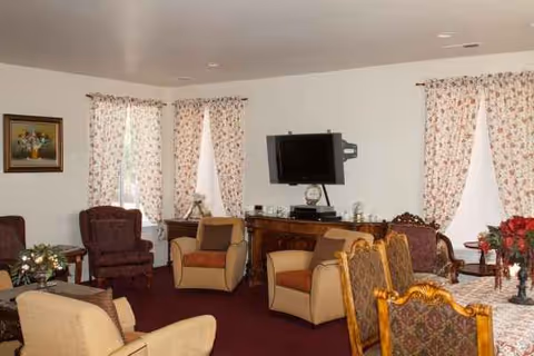 Bel Age senior living lounge with patterned chairs, floral curtains, and a wall-mounted TV.