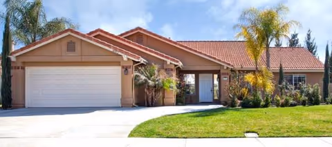 Single-story senior living home with a two-car garage, manicured lawn, and palm trees.