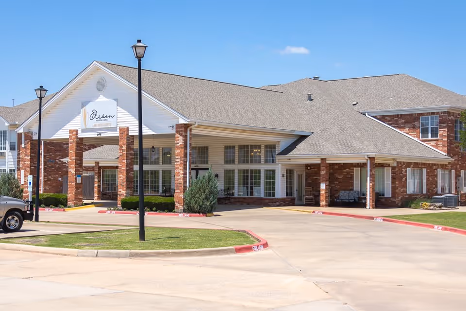 Exterior view of Elison Assisted Living of Lake Wellington building with brick and white siding, a covered entrance supported by brick columns, and a clear blue sky.