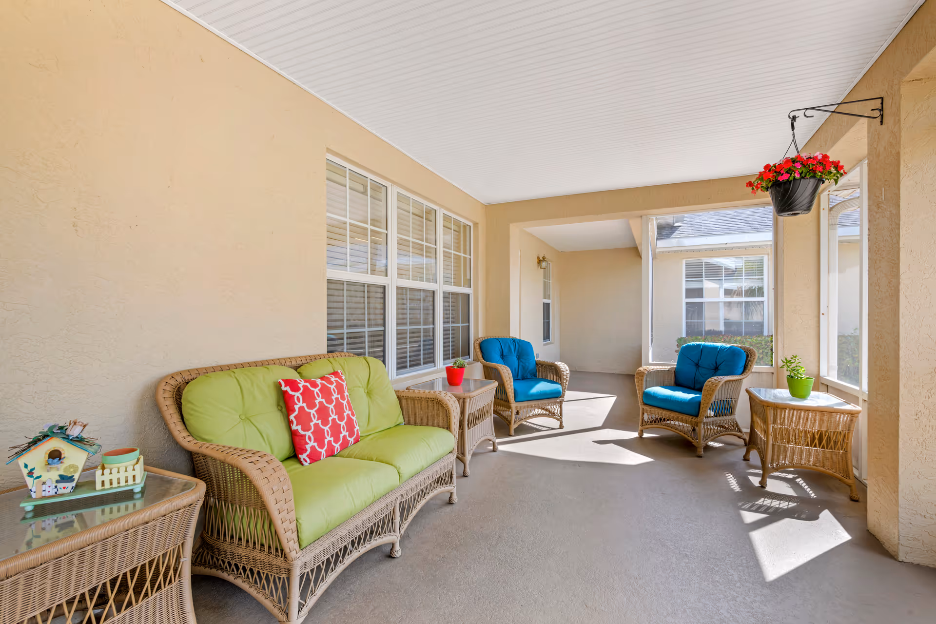 Covered patio with wicker seating, colorful cushions, and potted plants under a white ceiling.