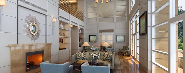 A spacious and well-lit living room area with high ceilings and large windows allowing natural light to fill the space. The room features a fireplace with a decorative mirror above it, built-in shelves with decorative items, comfortable seating including patterned and solid-colored chairs, and two table lamps on a central table. The floor is wooden, and there are framed artworks on the walls.