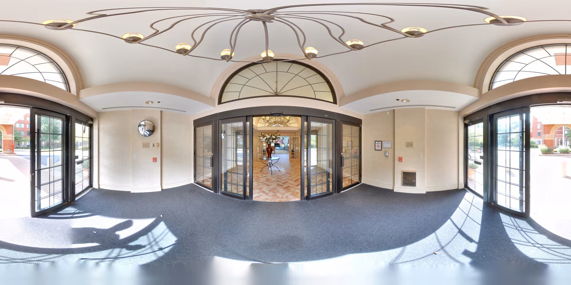 Spacious entrance lobby with glass double doors, arched transom windows, and a decorative chandelier