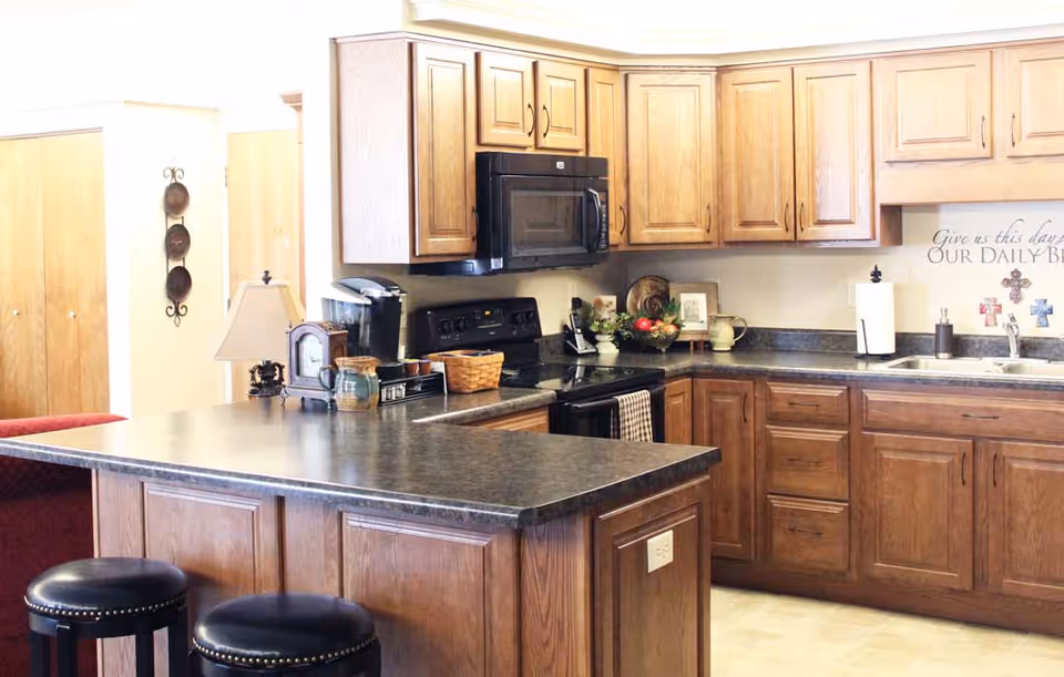 Bright kitchen with wooden cabinets, a large island with two stools, and black appliances and countertop items.
