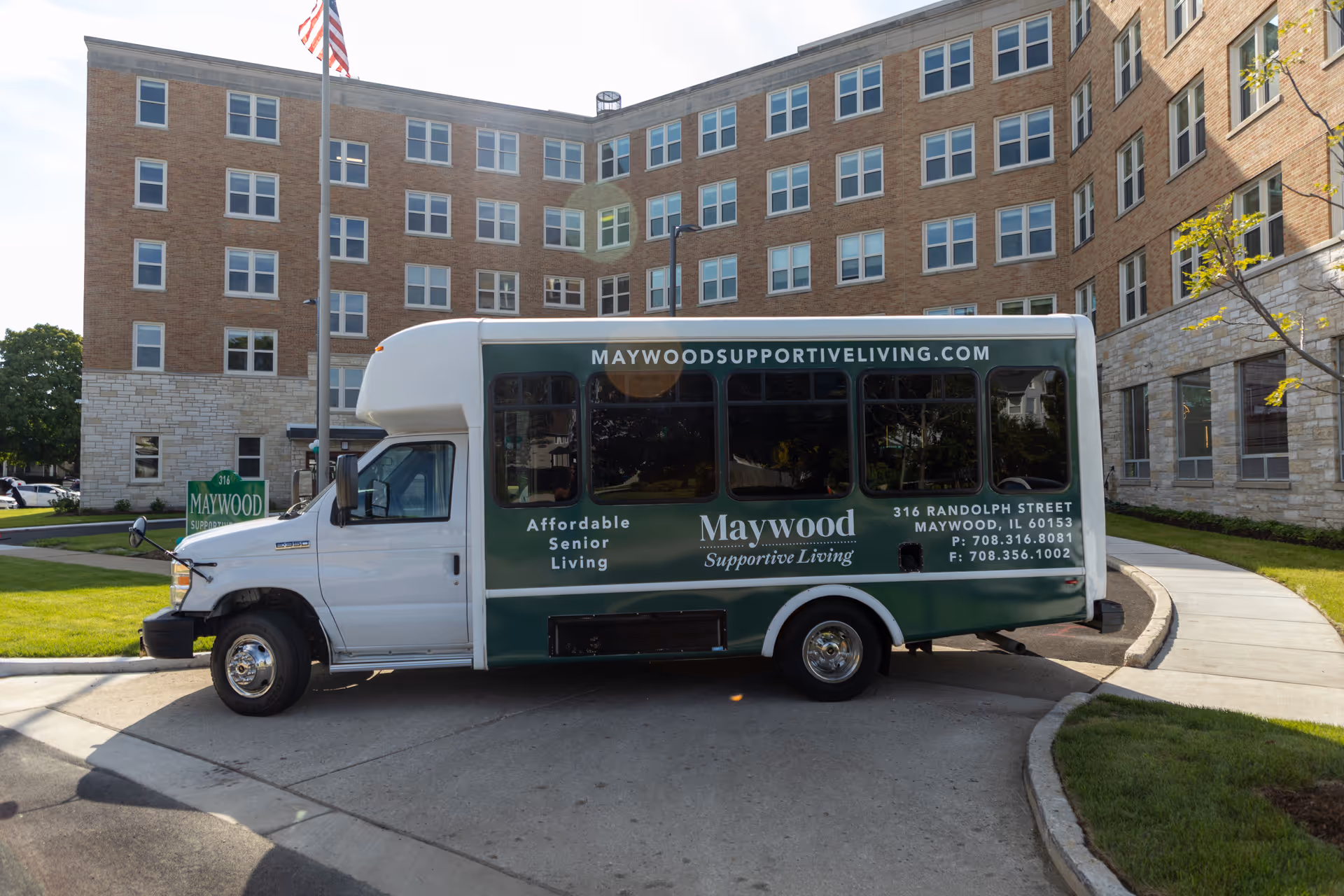 A Maywood Supportive Living shuttle bus parked in front of the Maywood senior living building.