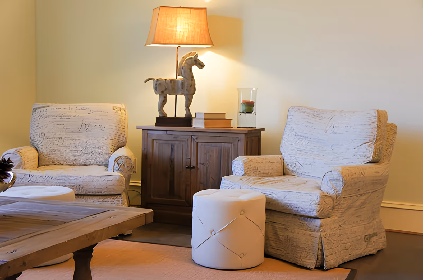 Two upholstered armchairs flank a wooden side table topped with a lamp and decorative horse statue in a cozy living room area.