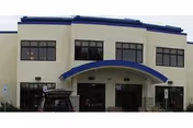 Front exterior view of a two-story building with large windows and a blue curved awning above the entrance. There is a vehicle parked in front of the building.