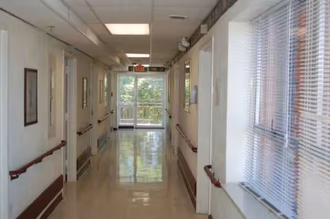 Bright corridor in a senior living facility with handrails, windows, and a glass exit door.