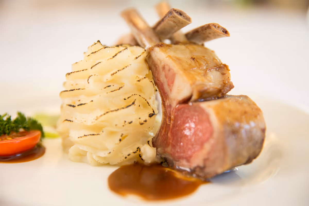 Close-up of a plated rack of lamb with mashed potatoes, sauce, and a small tomato garnish.