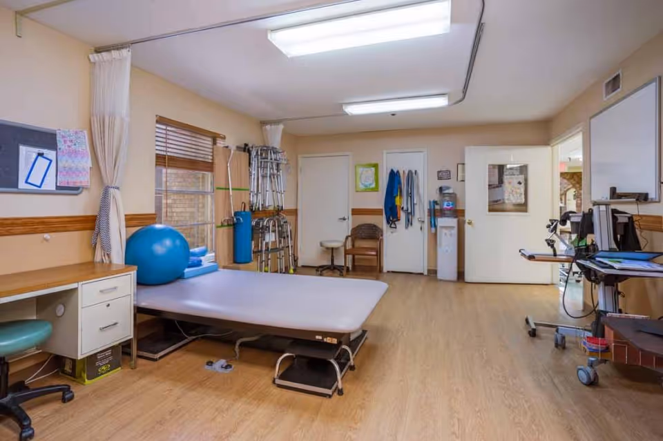 Rehabilitation therapy room with a treatment table, exercise ball, walkers and medical equipment in a senior facility.