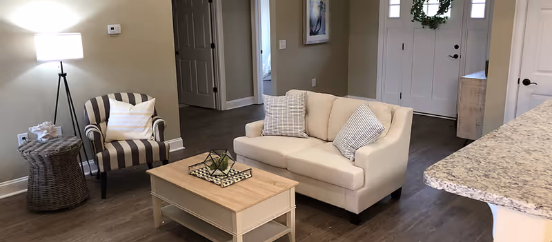 Living room with a beige loveseat, striped armchair, wooden coffee table, floor lamp, and front door in the background.