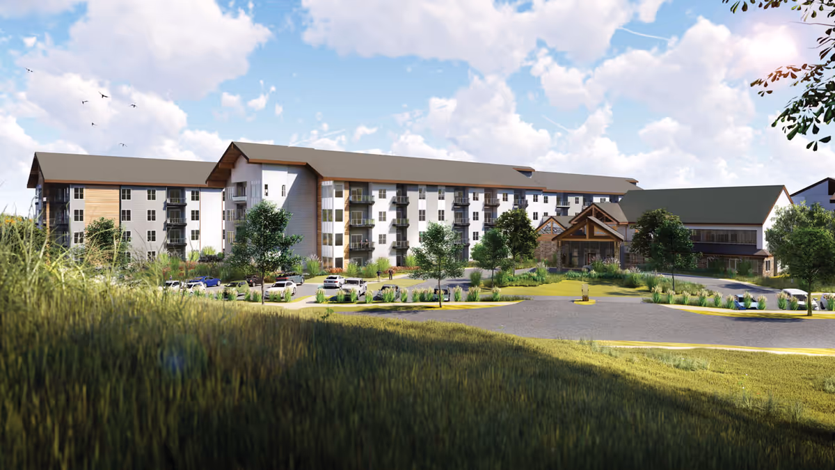 Exterior view of a large multi-story senior living facility building with a pitched roof, balconies, and a landscaped parking area in front under a partly cloudy sky.