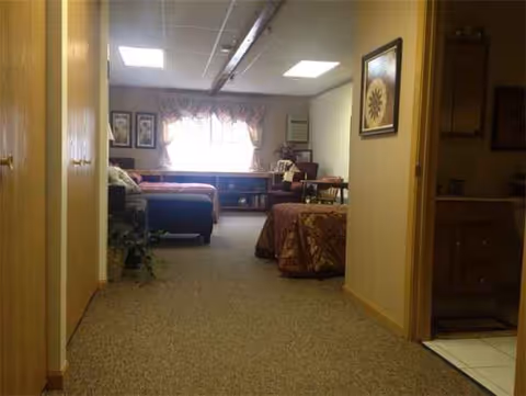 Interior hallway of a senior living facility with bedrooms and a sunlit common area