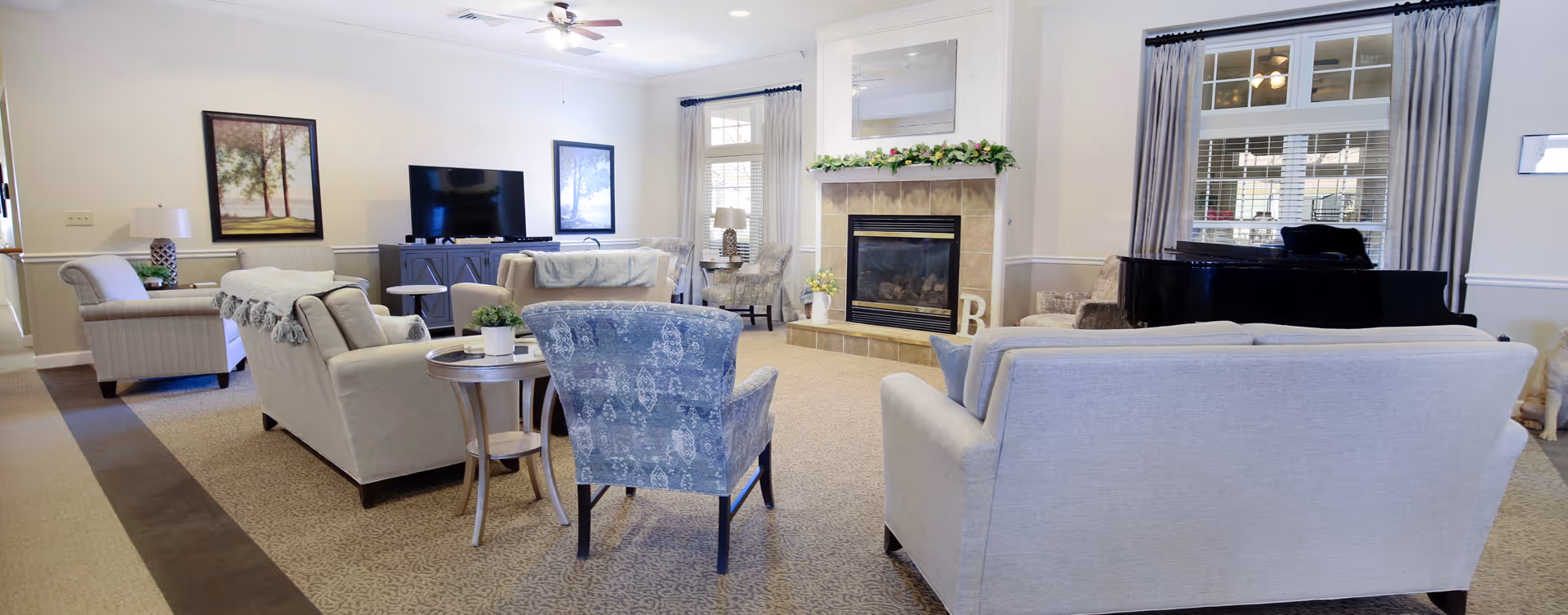 Communal living room with sofas and armchairs arranged around a fireplace and TV, with a piano by the window.