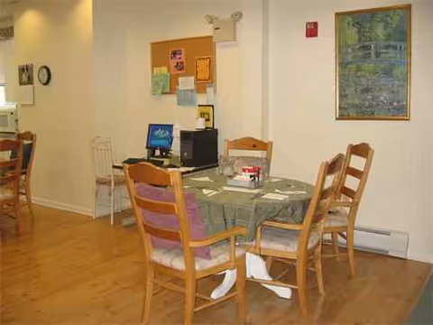 Round dining table with chairs and computer workstation in a bright senior living dining area.
