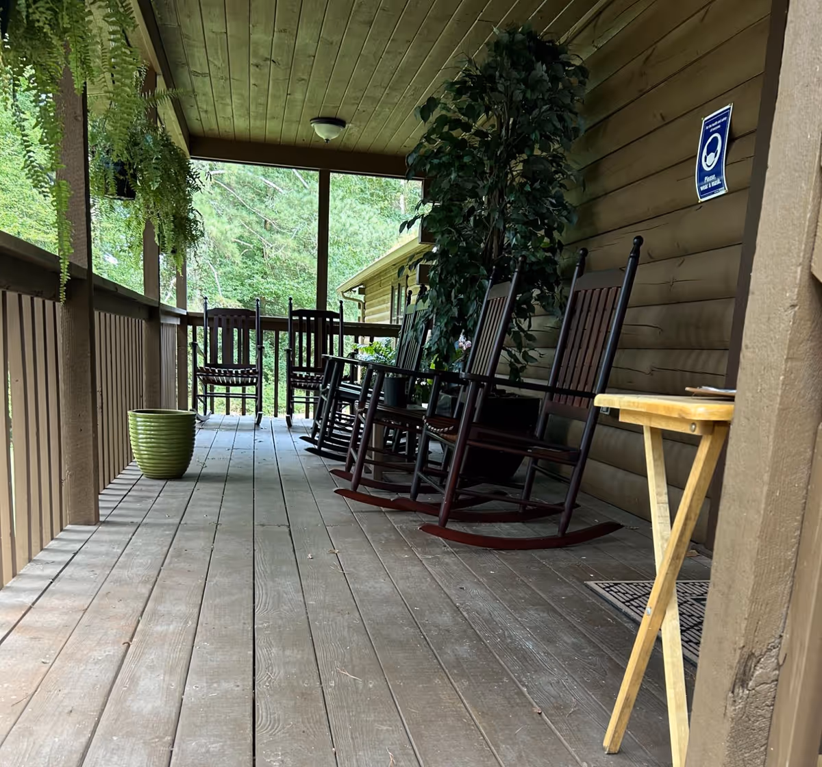 Covered wooden porch with several rocking chairs, potted plants, and a small folding table.
