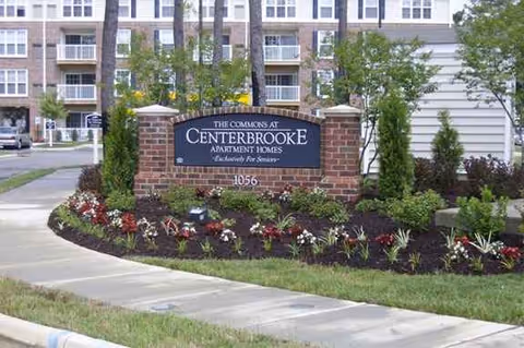 Brick sign reading The Commons at Centerbrooke Apartments with landscaping and building behind.
