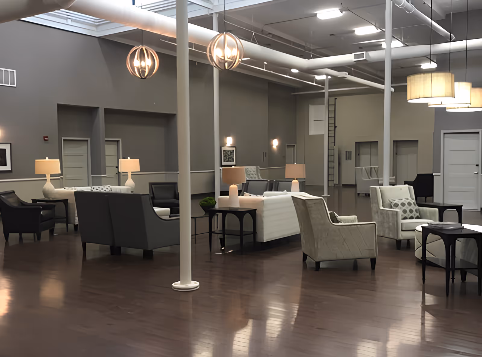 Spacious modern communal lounge with sofas, armchairs, side tables and pendant lights on polished hardwood floors.